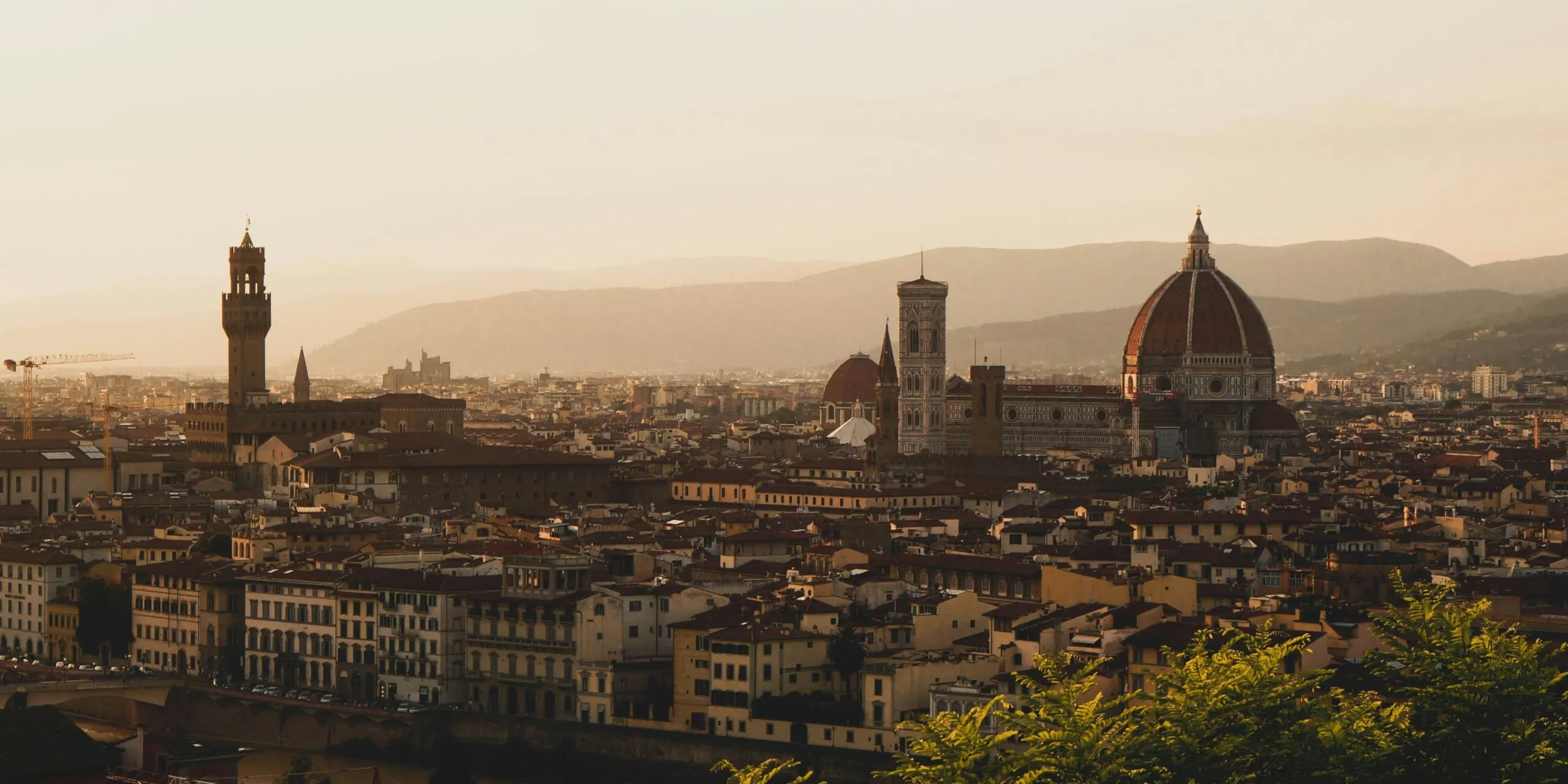 Florence skyline at sunset with the Duomo's red dome and the Palazzo Vecchio tower, golden light over city rooftops along the Arno.