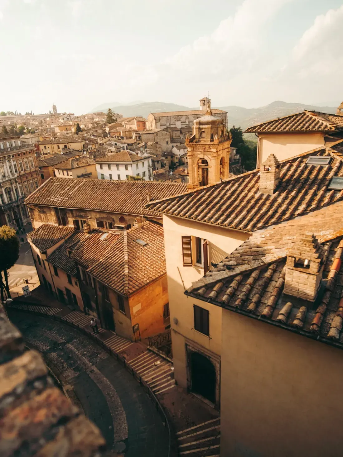 Sunlit Italian hill town with terracotta rooftops, narrow winding streets, and a central church bell tower, romantic Mediterranean scenery.